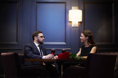 年轻的浪漫约会坐在桌子对面, 同时享受晚餐在餐厅的谈话