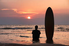 冲浪者独自坐在沙滩上冲浪后，在日落时分用冲浪板眺望大海