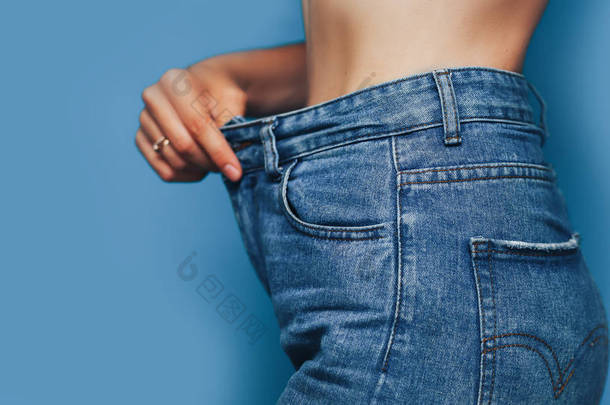 瘦女人的身体与宽松的裤子牛仔裤，轻重量的身体与宽松的衣服，苗条和健康的身体低脂肪的概念