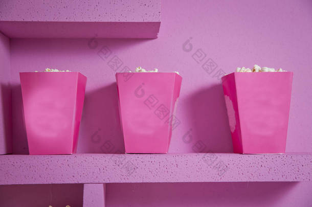 爆米花从条纹盒子溢出。三个复古风格的爆米花盒在嘉年华主题静物与街机游戏粉红色门票。一个宽大的经典盒剧院爆米花隔离在粉红色 .
