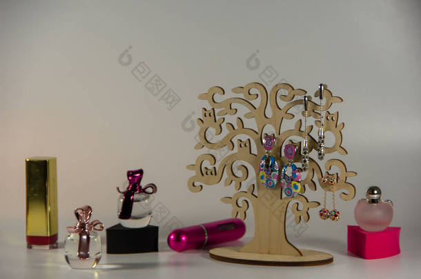 木制支架，三对长耳环，金色封闭口红，黑色和粉红色海绵，白色背景上带有芬芳香水的小瓶子.