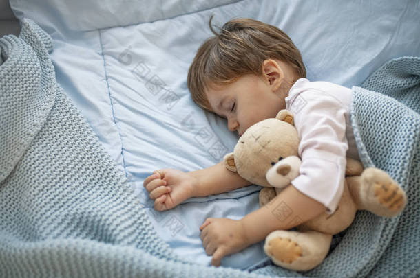健康的孩子，最甜美的金发幼儿男孩在床上抱着她的泰迪熊<strong>睡</strong>觉。可爱的蹒跚学步的女孩在灰色的床上<strong>小睡</strong>，抱着她的泰迪熊。婴儿幼儿<strong>睡</strong>着了与泰迪熊