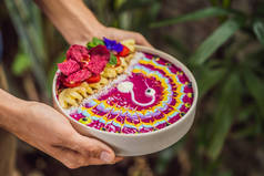 年轻人吃着冥想式早餐，吃着健康的热带早餐，带热带水果的圆滑碗，装饰着五彩斑斓的带有姜黄和螺旋藻的酸奶图案。 它也是