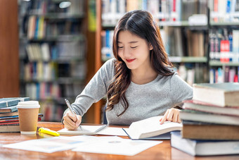 亚洲青年学生穿着休闲服在大学图书馆阅读和做作业，或与各种书籍和固定在书架背景的木桌上，回到学校图片