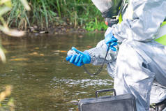 specialist in a protective suit and mask, is measuring the device on the pond, holding it in his han