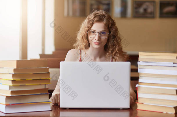 紧贴着学习和使用新技术的少女的门廊，坐在敞开的白膝顶上的桌子前，女士穿着T恤衫，学生们被不同的书包围着。 教育概念.