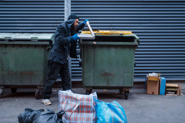 满嘴胡子的肮脏乞丐在街上的垃圾桶里找到了披萨。 贫穷是一个社会问题，无家可归、孤独、酗酒、酗酒、城市孤独