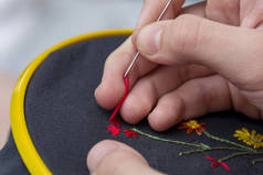 一个女孩/女人/女人的手用黄色的小塑料框缝制一个小绣花图案。 背景为针织叶型、绣花型、边框和多色螺纹.