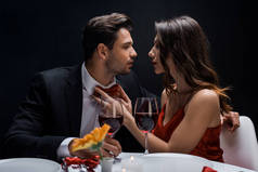 在与黑人隔离的浪漫晚餐中，美女调整英俊男人的领结的侧视图