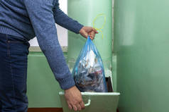在俄罗斯,把垃圾扔进垃圾箱. 一个人把垃圾扔进蓝色的塑料袋里. 旧的多层楼房.