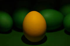 一只黄色彩绘的复活节彩蛋站在绿色彩蛋前面，背景是绿色的.