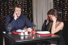 在餐馆的一张桌子旁，一对矛盾的夫妇。男人用智能手机说话，女人惹恼了.