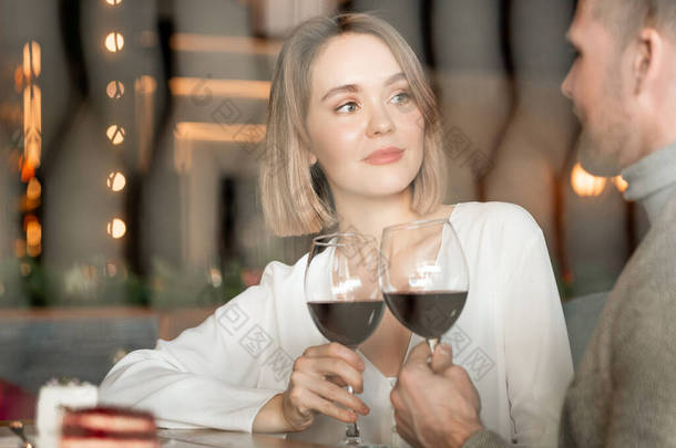 <strong>坐在餐馆</strong>里的迷人的白人妇女和男子的横向画像，他们的眼镜上挂着红葡萄酒