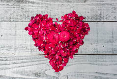 粉红玫瑰花瓣的特写镜头，心形，白色木制桌面，情人节概念