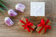 有红丝带和美丽的丁香郁金香在木板上的礼品盒。顶部视图。假日送礼的概念.
