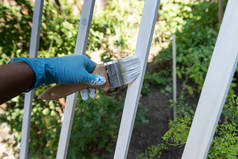 手拿着涂有白色油漆的刷子，油漆可以把木板涂在院子的深色背景上