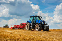 蓝色的新型拖拉机，田里有红色的犁头，天空阴云密布，农业机械在运转