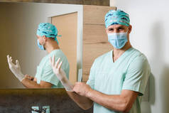 微笑的外科医生把无菌的医疗手套放在他的手上，并对着镜头看。手部卫生对大肠埃希菌病的保护