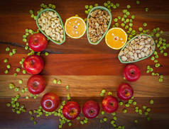 苹果、橙子、开心果、核桃、腰果和芥末豌豆放在木桌上.顶部视图