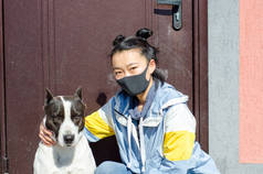 年轻的韩国女孩戴着防护面罩，看着狗也戴着医疗面罩。COVID-19对宠物的概念是危险的
