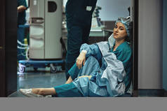 累了的医生在医院走廊里做完手术后坐着。医生和医生的沉重负担。下班后休息。流行病、缺乏医务人员、医疗病房.