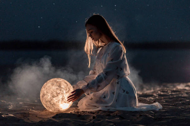 美丽的小女孩在沙滩上，手里拿着沙子和星星，手里拿着月亮