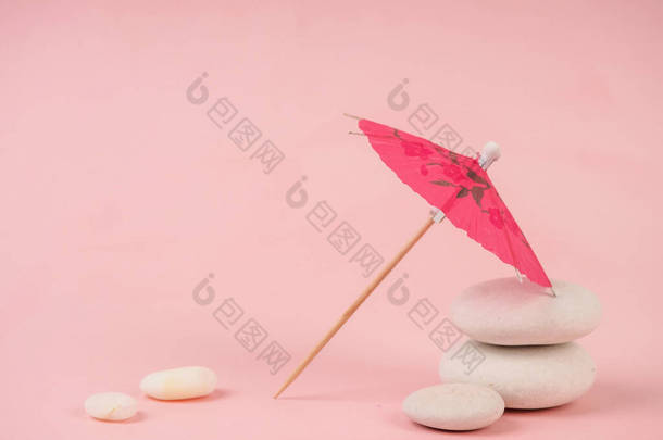 鸡尾酒尾伞。粉红纸制鸡尾酒伞,粉红色孤立.粉红石头上的纸制粉红伞，靠近白色石头，休闲和简约的概念.