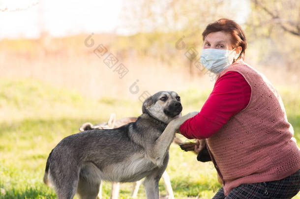 戴着医疗面罩的女志愿者和无家可归的狗站在户外。志愿服务和动物收容所的概念。当你有狗的时候会更孤独