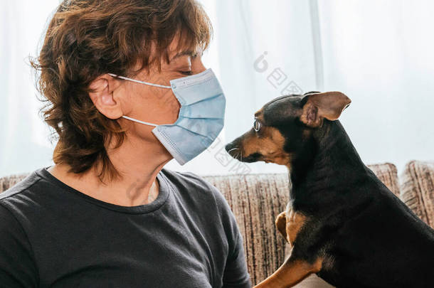 女人坐在客厅里，戴着口罩，<strong>抵御</strong>考罗奈德、眼镜蛇或任何其他疾病，惊讶地嗅着她的狗