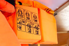 橙色的救生衣在船上，特写在使用说明上，详细说明如何穿上，穿上救生衣，浅浅的涂抹。个人浮力装置、信息图片、浮力服、浮力辅助装置