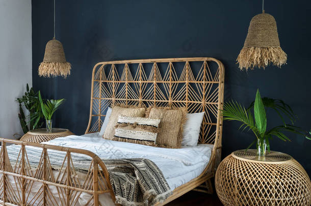 波希米亚风格的室内舒适的房子与少数民族装饰。精致的卧室，床头柜上方点着灯，舒适的床上有枕头，有仙人掌植物，<strong>还有</strong>深蓝色墙壁上的空间