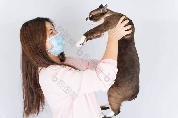 亚洲美丽的快乐女人，戴着医疗保护面罩，保护头牛，过滤灰尘PM 2.5，<strong>感冒</strong>，对猫毛过敏，还带着一只白色背景的猫