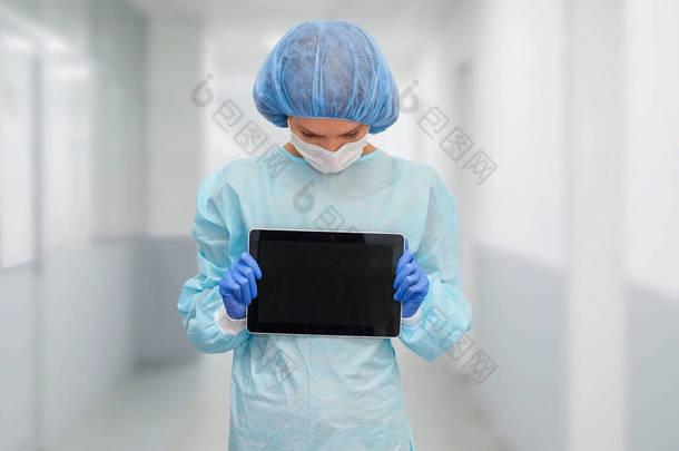 身着防护服的女<strong>医生</strong>：医疗面罩、<strong>帽子</strong>和长袍。这名妇女使用数字平板电脑，并在屏幕上显示疾病统计数据.