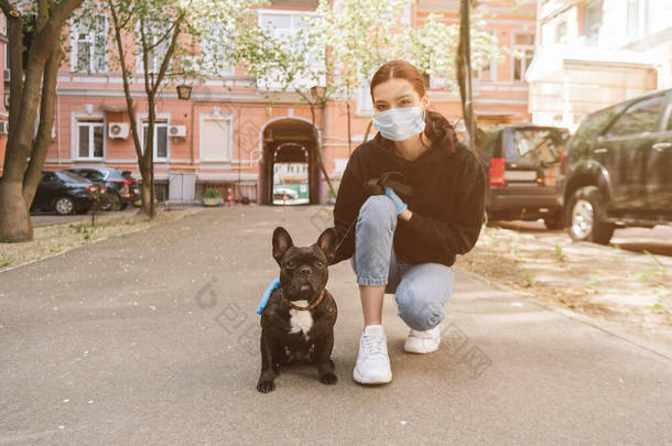 戴着医疗面罩和乳胶手套在街上摸可爱的法国斗牛犬的女人 