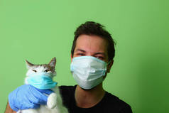 那只猫在一个戴外科医疗面具的男人手里。绿色背景爱护动物的概念