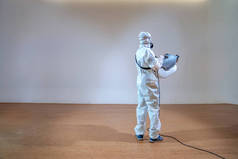 穿着防护服的专业技术人员在木地板和白色背景上使用电喷机喷洒灭菌液，并配以工作室光.