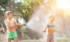 两个孩子在花园里玩耍，从软管里相互倾盆大雨。快乐童年和炎热夏日活动的概念形象.