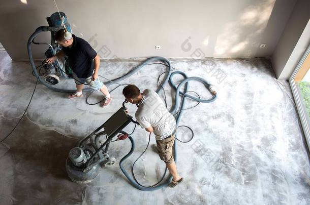 在应用环氧树脂地板之前，在家庭起居室里的建筑工人在研磨混凝土表面。聚氨酯和环氧树脂地板。.