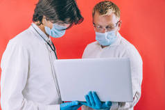 两名戴着蓝色手套的医生，脸上戴着口罩，背景是红色的笔记本电脑