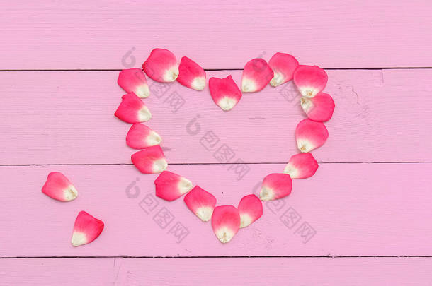 用玫瑰花瓣在粉色木板上做成的浅粉色的心。浪漫柔和的背景。复制垃圾邮件.