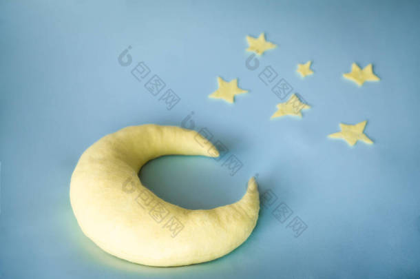 可爱的手工制作的枕头形状的月亮在蓝天背景与感觉到的星星，特写。月球枕头和星星，用来把新生儿放在床上