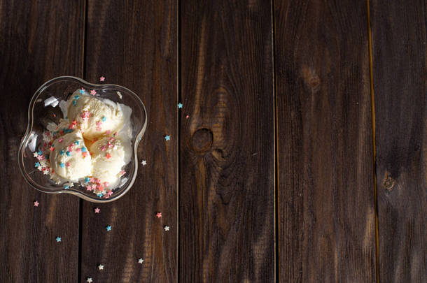 白色的香草冰淇淋球，在<strong>色彩艳丽</strong>的洒水下，放在一个甜点碗里。深色木桌上装饰过的冰淇淋.