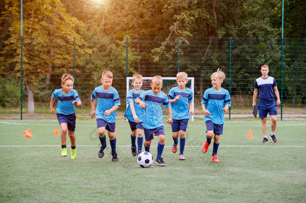 在足球训练前，儿童队在<strong>升温</strong>的情况下跑动和踢足球。背景教练观察训练过程