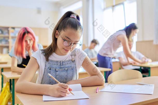 十几岁的孩子在<strong>课</strong>堂上，坐在前排的女孩坐在<strong>写字</strong>台前，用笔记本<strong>写字</strong>