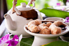 下午茶放在瓷壶里，奶油饼干放在花和绿叶桌子上装饰