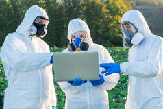 身穿白色防护装备、戴着化学面罩和眼镜的科学家和农艺学家在农田里使用笔记本电脑.
