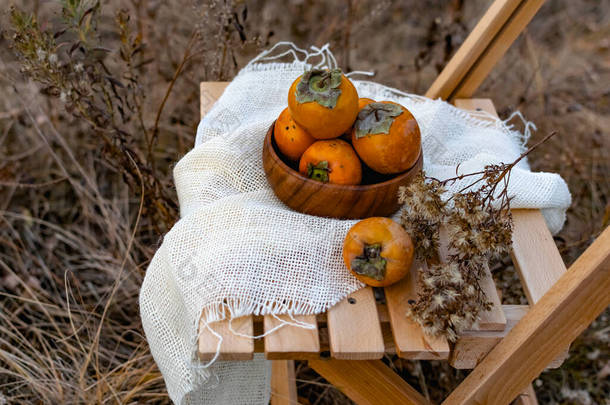 科罗洛克品种的甜蕨类水果的秋天组成，在一个木制盘子里，在一个木制凳子上，用一块麻布装饰着干枯的花朵。背景上,秋天的树木,干枯的青草