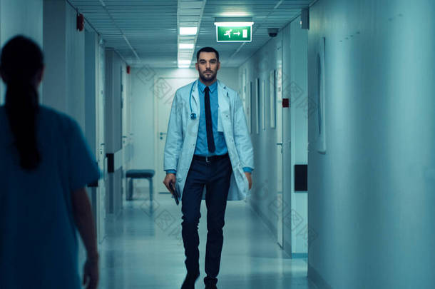 有决心的英俊医生身穿白衣，头戴听诊器步行穿过医院走廊。配备专业人员的现代明快诊所.