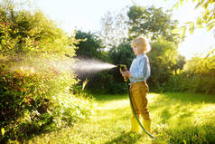 有趣的小男孩浇灌植物，在阳光灿烂的后院玩花园软管。学龄前儿童与喷水为乐.青少年暑期户外活动.