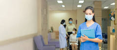 女医务人员或医生戴着口罩，拿着病人的治疗档案站在走廊里，而医院里的氛围却充满了人.